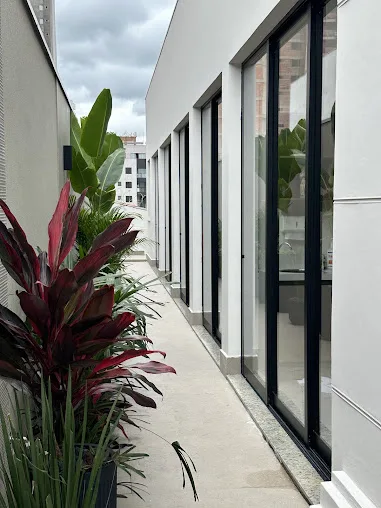 Circulação externa com vidros e vegetação ao lado das salas de atendimento